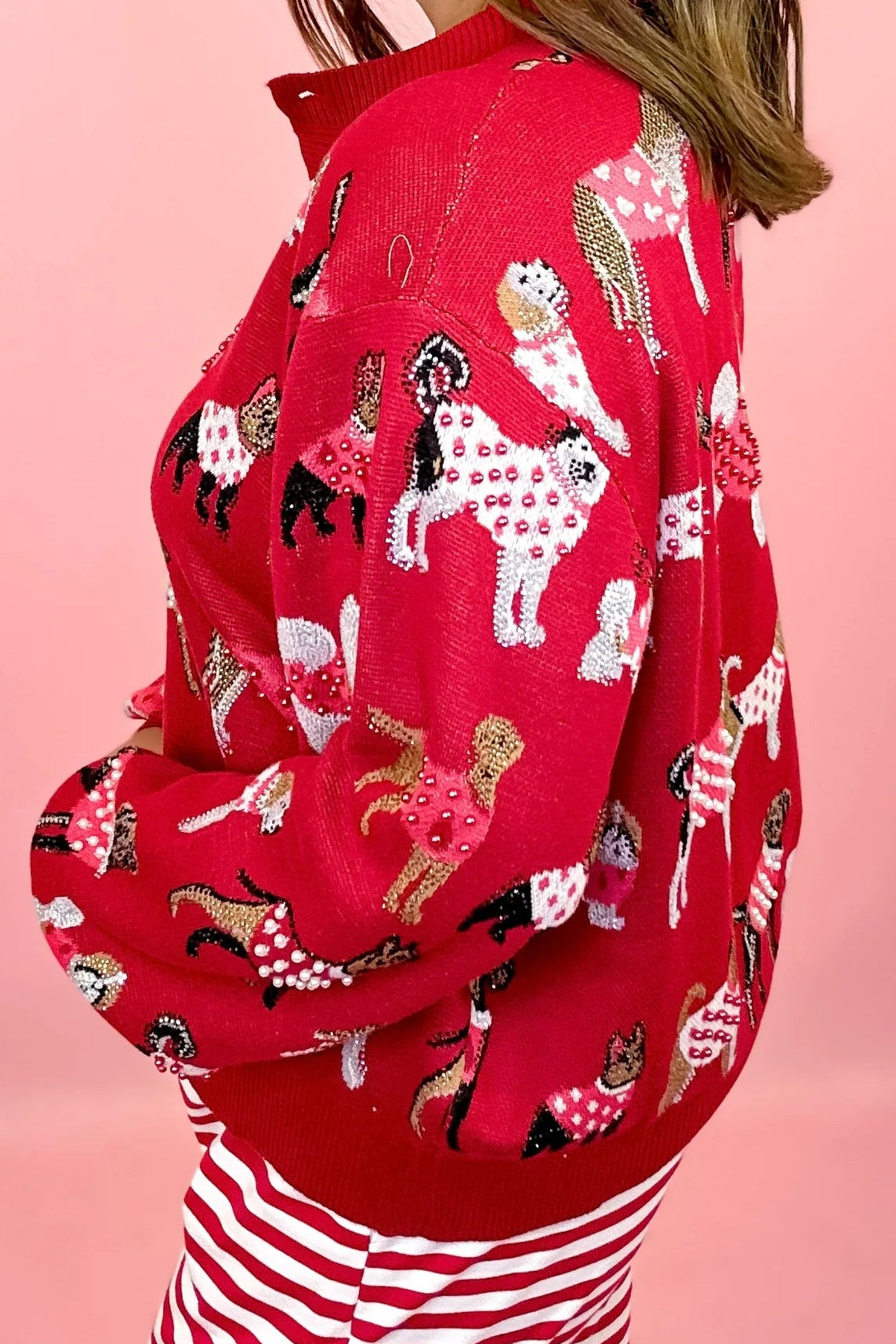 A woman wearing a red button cardigan. A woman wearing a festive Queen of Sparkles knit cardigan with dogs wearing sweaters all over print on the cardigan, Embellished with Crystals and sequins and pearls
