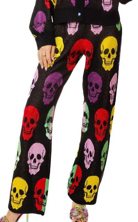 A woman modeling a matching black knit cardigan and wide-leg pants set with a colorful all-over skull print, photographed against a plain white background.