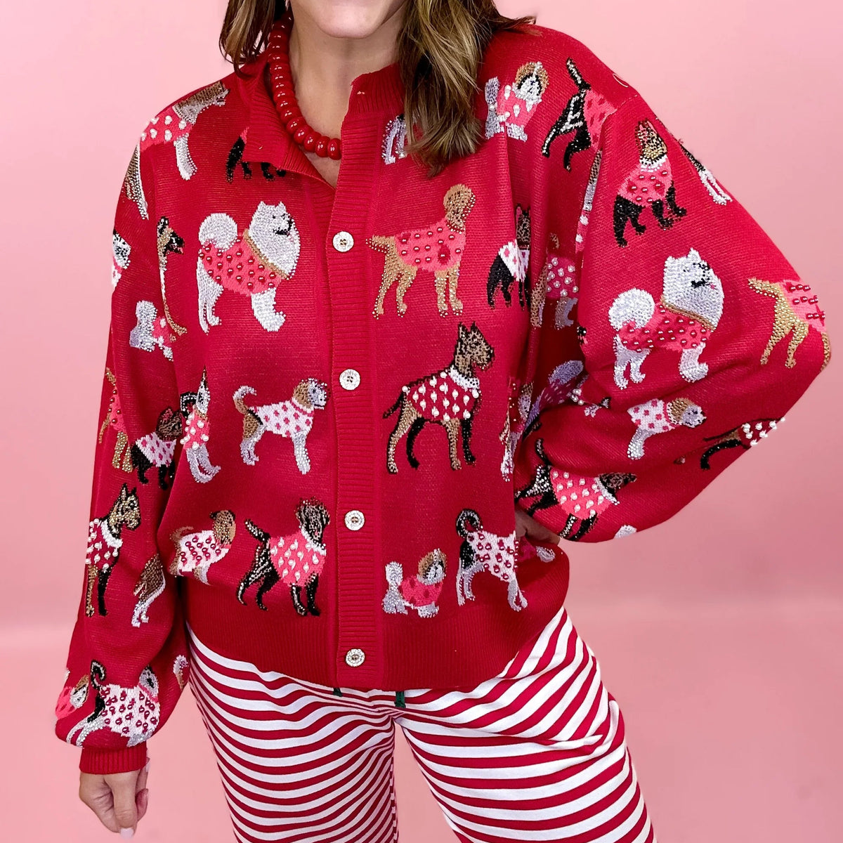 A woman  wearing a festive Queen of Sparkles knit cardigan a featuring dogs wearing sweaters all over print on the cardigan, Embellished with Crystals and sequins