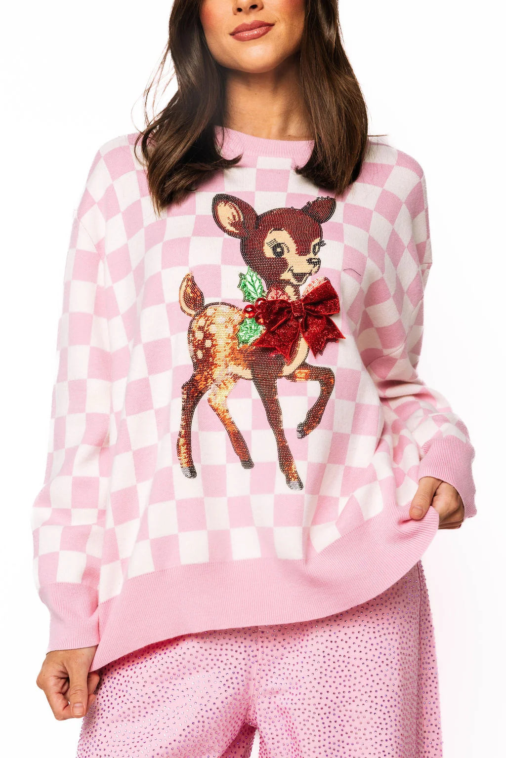 


A woman wearing a queen of sparkles pink and white checkered sweater with a sequined vintage Christmas style deer graphic on the front,  a 3d Red bow and crystal jewels