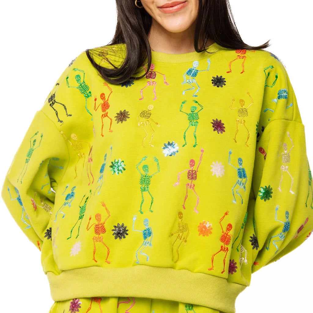 A model wearing a bright lime green matching lounge set featuring a sweatshirt and shorts, both decorated with colorful embroidered figures and motifs, against a plain white background.